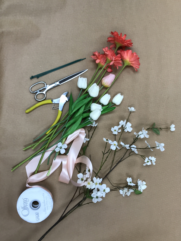 Materials for wreath laid out; pink ribbon, white flowers, scissors, and wire cutters.