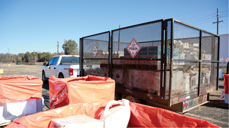 A pickup truck with a large, enclosed trailer sits at a collection location. The trailer has hazard placard with the word "POISON."