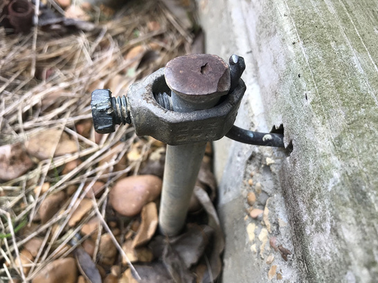 A steel rod driven into the ground and attached by a large lug to a wire coming from a concrete wall.