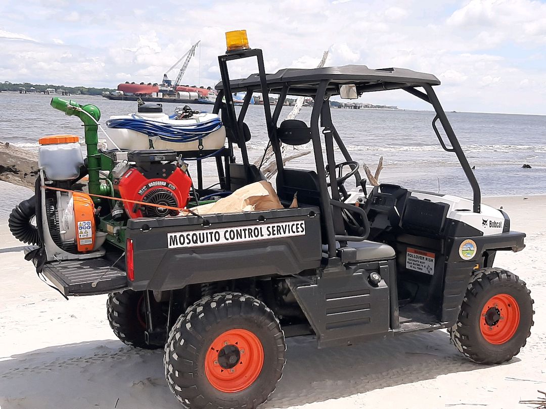ATV on a beach with a machine to spray mosquito repellant on the back.