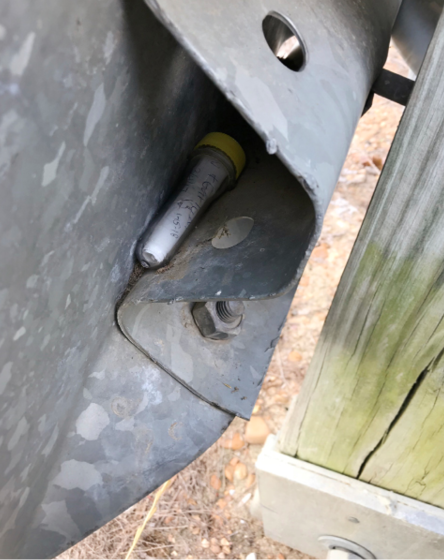 A small clear tube (geocache) tucked into the back of a metal sign.