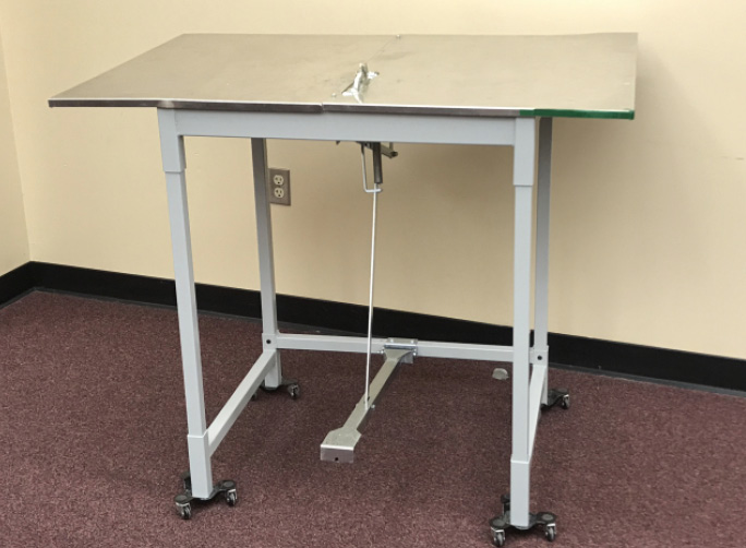 A work table on wheels with an attached pedal.