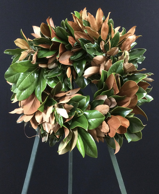 A finished magnolia wreath on a stand. The leaves are placed so that some show the glossy green sides and some the leathery brown sides.