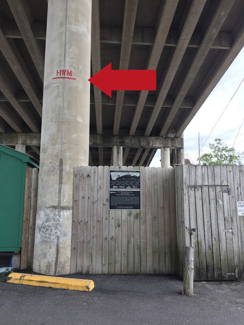 A concrete beam under a highway overpass with a line indicating the high water mark from Hurricane Katrina.