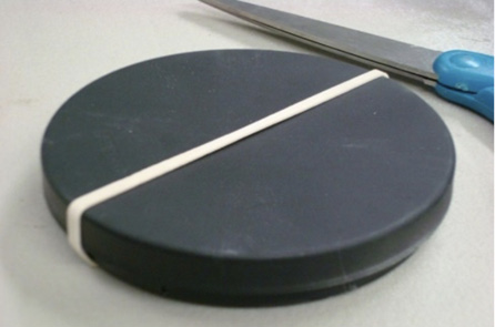 A round, black tray with its top held on with a rubber band.