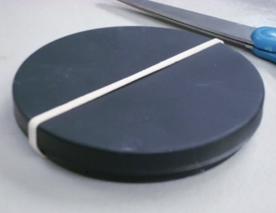 A round, black tray with its top held on with a rubber band.