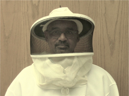 A person wearing a hat with a screen veil over their face. The bottom part of the veil is attached to a jacket the person is wearing.