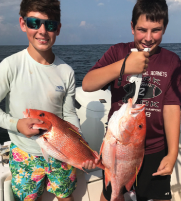 Two boys pose on a boat in the ocean, each holding a large red-orange fish. One fish has one yellow tag attached to its back, and the other fish has two tags.