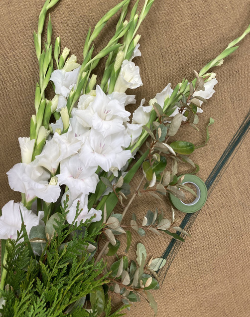 A bunch of white flowers, greenery, wire, and a roll of tape on a brown background.