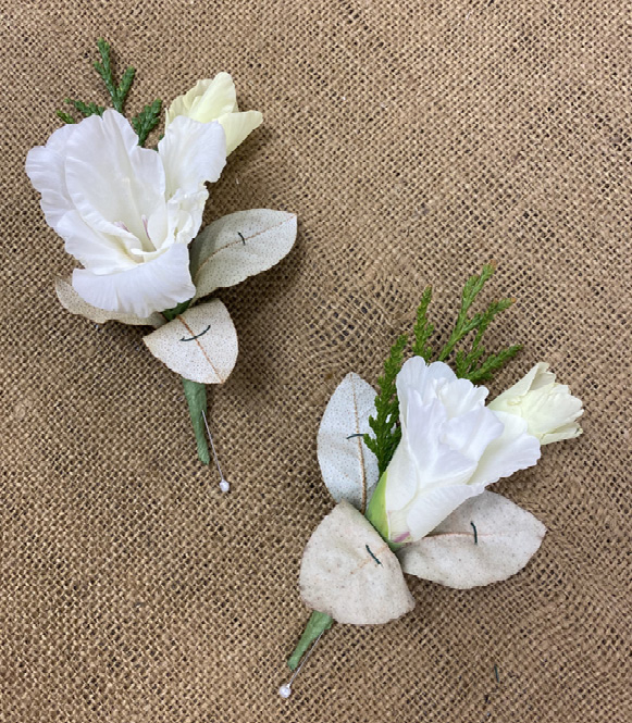 Two white flowers with sprigs of greenery and three small leaves attached together. The leaves have very small, single stitches of wire holding them in place.