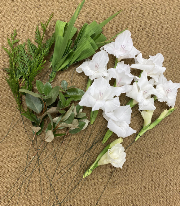 Three types of greenery and several white flowers attached to wires.