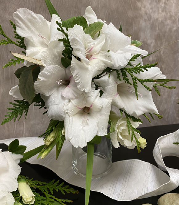 A bouquet of white flowers and small pieces of greenery in a glass vase.