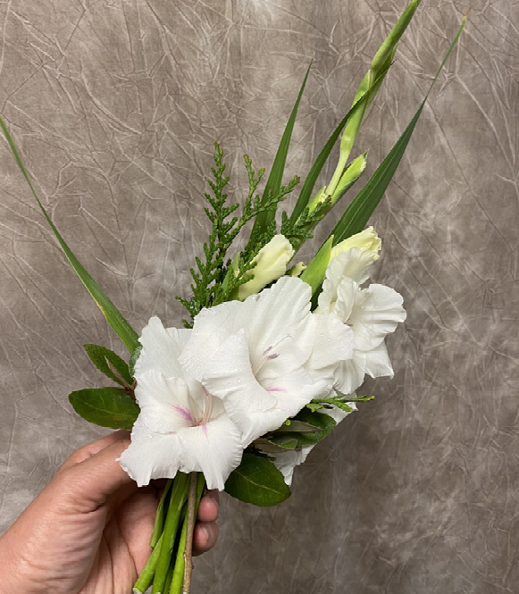 A person’s hand holds a small bouquet of white flowers and greenery.