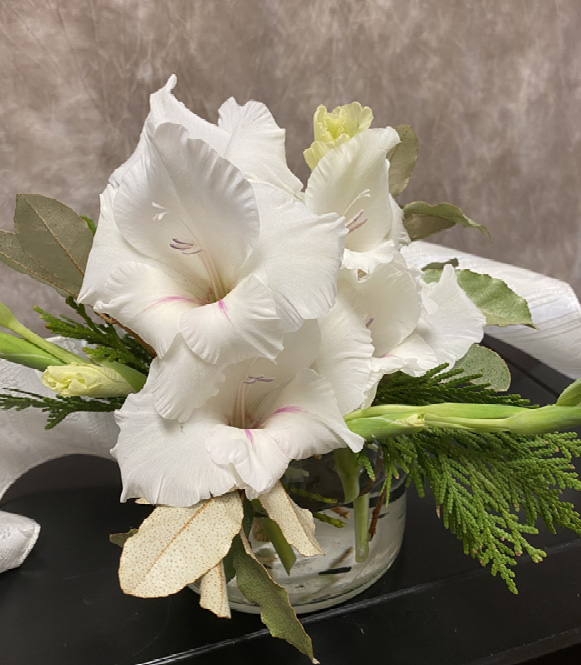 A short glass vase with a small bouquet of white flowers and greenery.