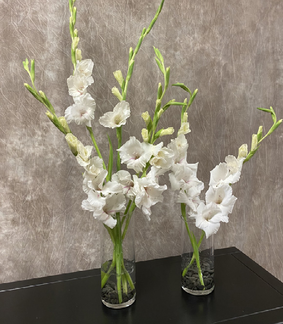 Two small glass vases with dark rocks and three or four stalks of white flowers in each vase.