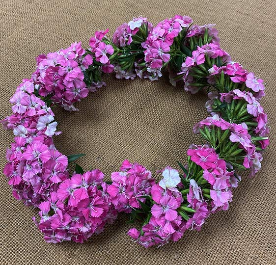 Flower crown with small pink dianthus blooms displayed on burlap cloth.
