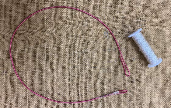 Pink floral wire bent into large, opened loop displayed on burlap cloth next to spool of thread.
