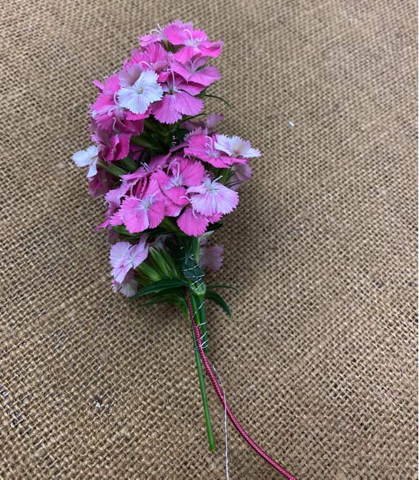 Floral wire is shown with small dianthus blooms added to the end and secured with thread on burlap cloth.
