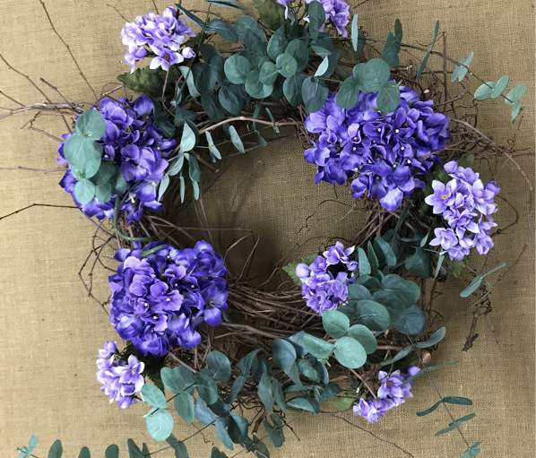 A partly completed wreath features eucalyptus stems molded and shaped to follow a clockwise rotation around the floral design.
