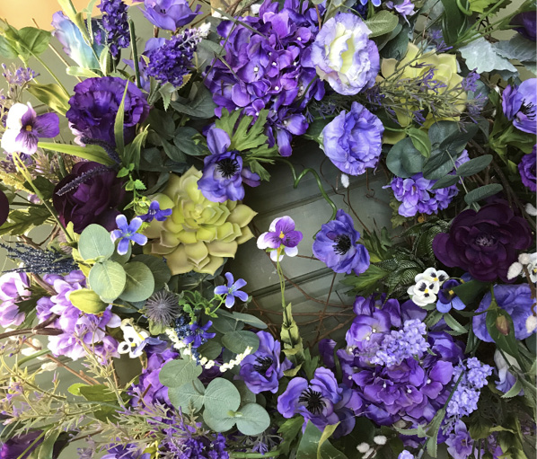 A half-completed wreath features contrasting colors, foliage of varying sizes and varying lengths of florals following a circular motion. 