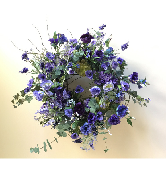 The completed silk floral wreath features hydrangeas, eucalyptus stems, Eustomas and more. The foundation made of grapevine cane is nearly invisible from the front. Sellers should photograph the final design on a neutral background.
