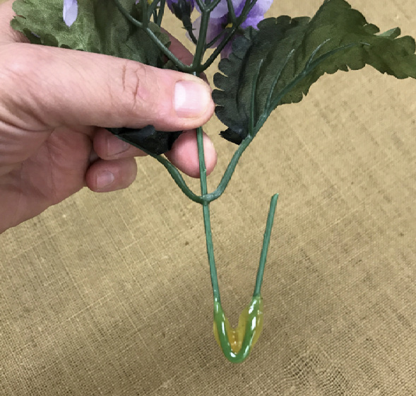A demonstration of how to properly prepare a stem for a wreath. A silk floral piece will adhere to a wreath more securely when the stem is bent into a u-shape and dipped into the glue.
