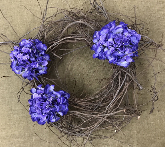 A grapevine wreath has three large silk hydrangeas placed in asymmetrically to give the design a more organic look.