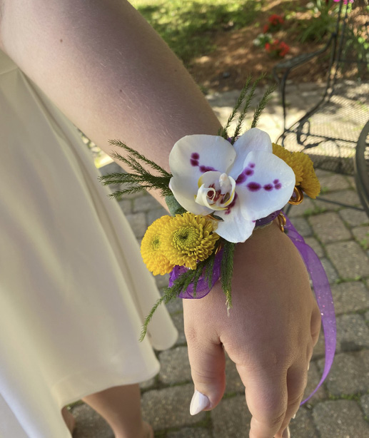 A hand is extended to display the completed flower bracelet as it would naturally fit on a wrist.