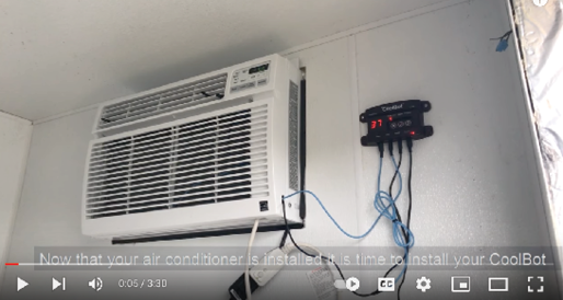Screen capture from a video showing an air conditioner in a wall with a controller mounted near it.