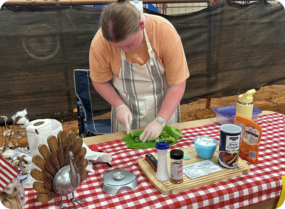 A contestant cuts peppers on a decorated table with many other ingredients.