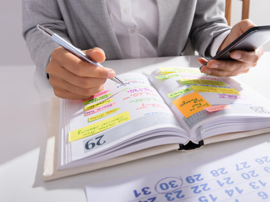 Person’s hands hold a mobile phone with a list of work on the desk.