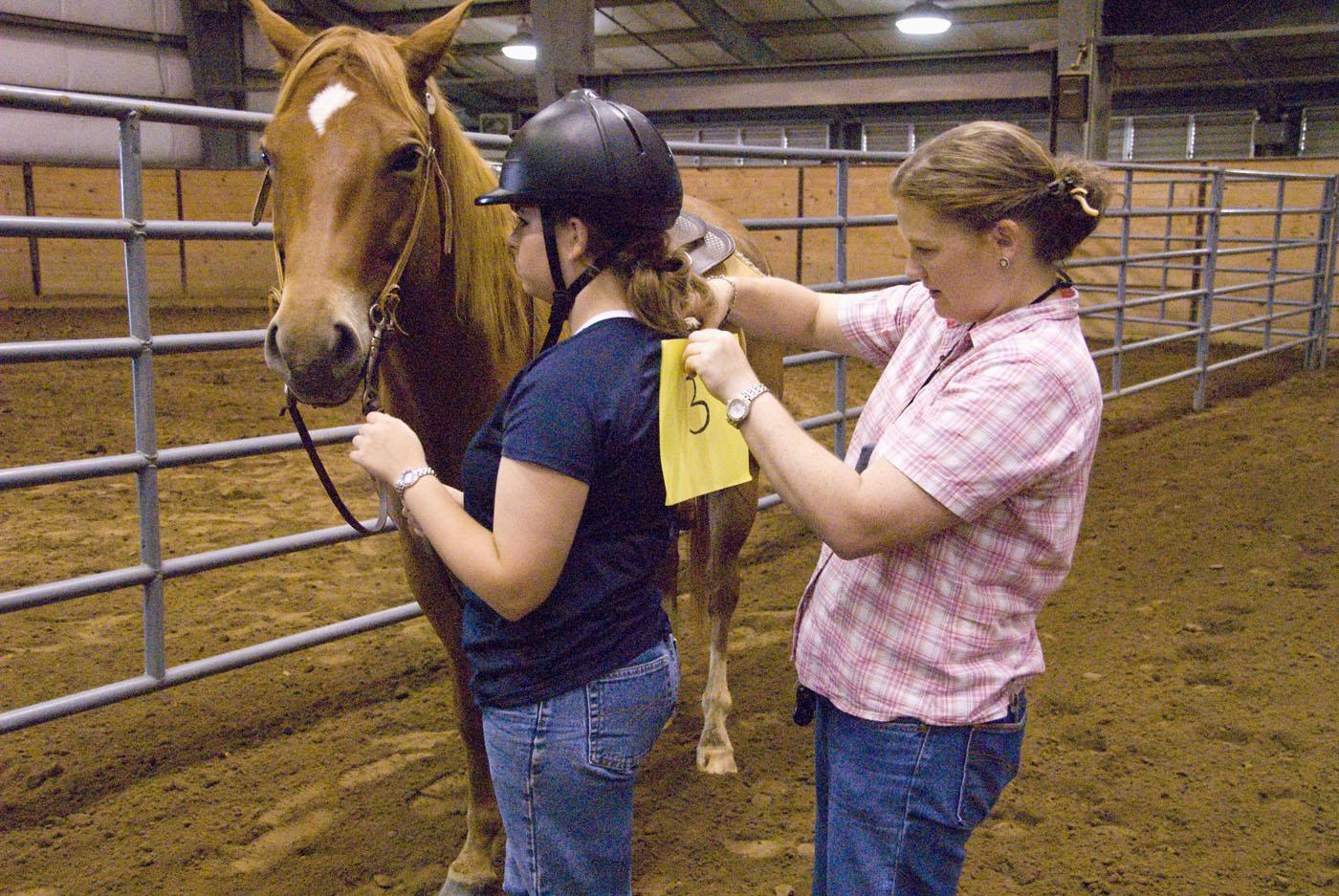 Mississippi State University equestrian team member Megan Dorris, left, steadies her mount while coach Molly Nicodemus pins on her number before an equitation demonstration. (Photo by Marco Nicovich)