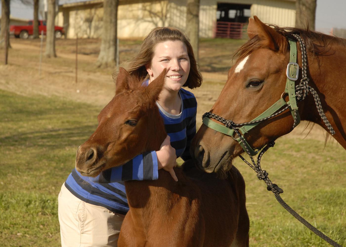 Dr. Joy Mordecai, an equine reproduction resident at Mississippi State University's College of Veterinary Medicine, holds Freddie Mac, one of the twin foals from a champion cutting horse, while its surrogate mother keeps a close eye on her colt. (Photo by Linda Breazeale)