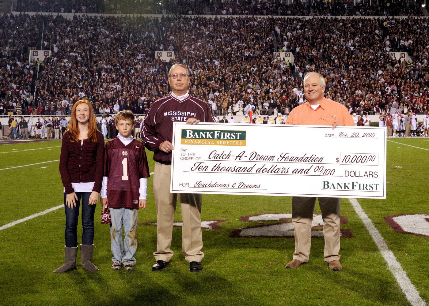 BankFirst made a donation to the Catch-A-Dream Foundation every time the Mississippi State University Bulldogs scored touchdowns. BankFirst's Jerry Wilson, left, presents a ceremonial check for $10,000 to Marty Brunson at the MSU-Arkansas game Nov. 20. Wilson is accompanied by his grandchildren, Mauri and Miller Wilson. (Photo by MSU Ag Communications/Kat Lawrence)
