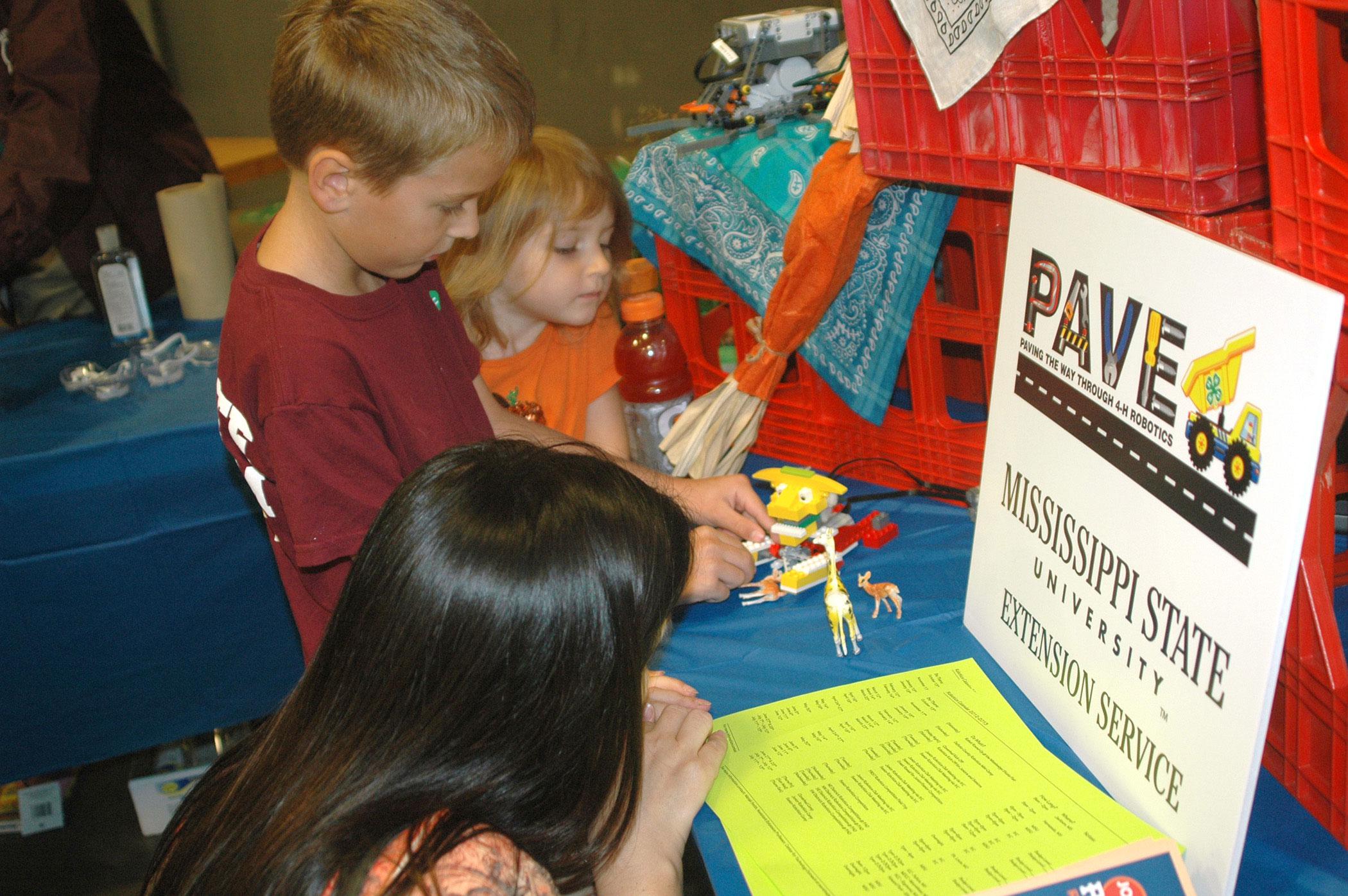 Monica Morel, Hancock County robotics club volunteer leader, helps Luke and Rebekah Schilling of Oktibbeha County with a robot during 4-H Day at the Mississippi State Fair in Jackson on Oct. 13. The robotics exhibit was one of several hands-on science activities available to visitors. (Photo by MSU Ag Communications/Susan Collins-Smith)