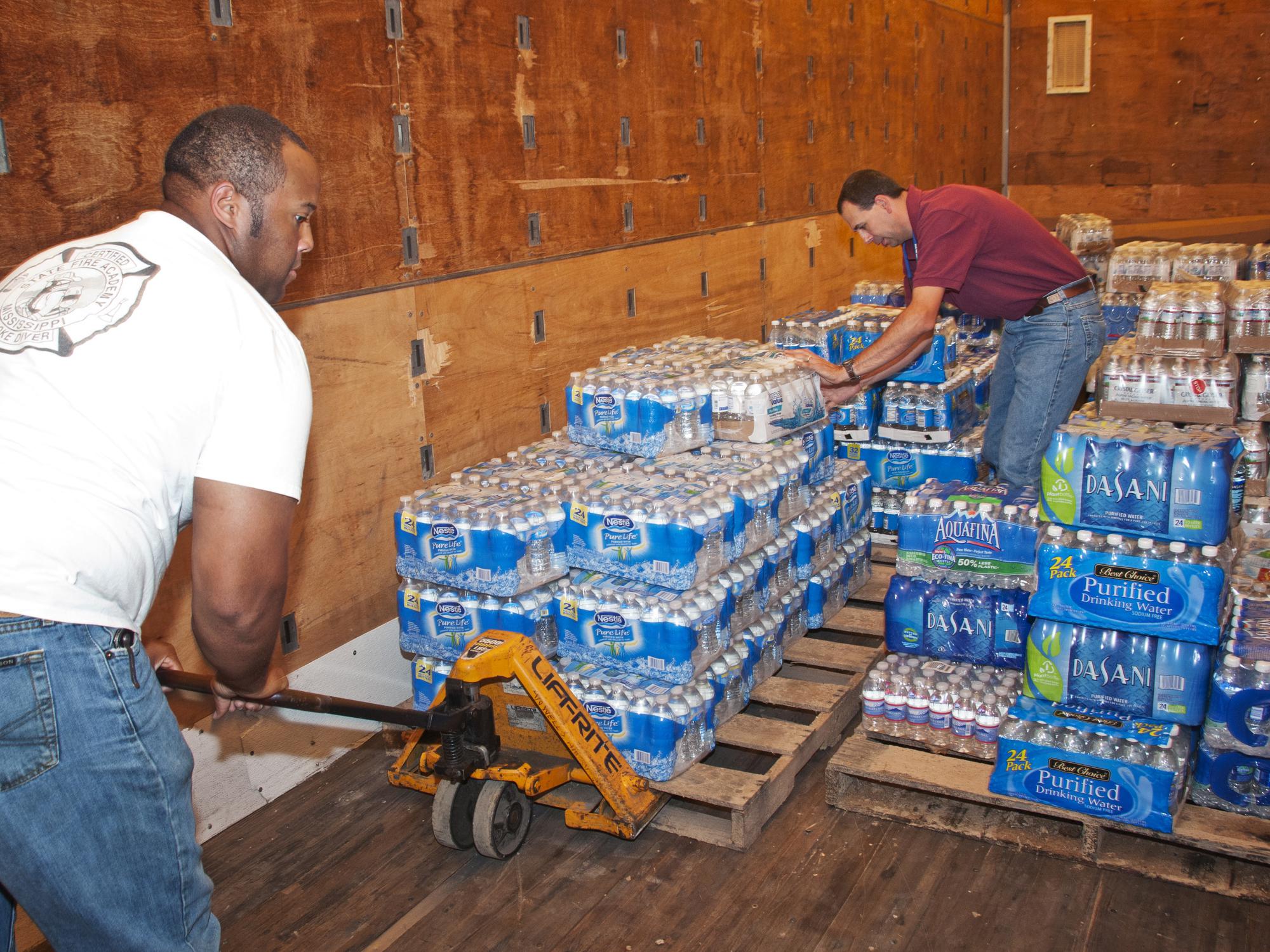 Two men move cases of bottled water in a storehouse.