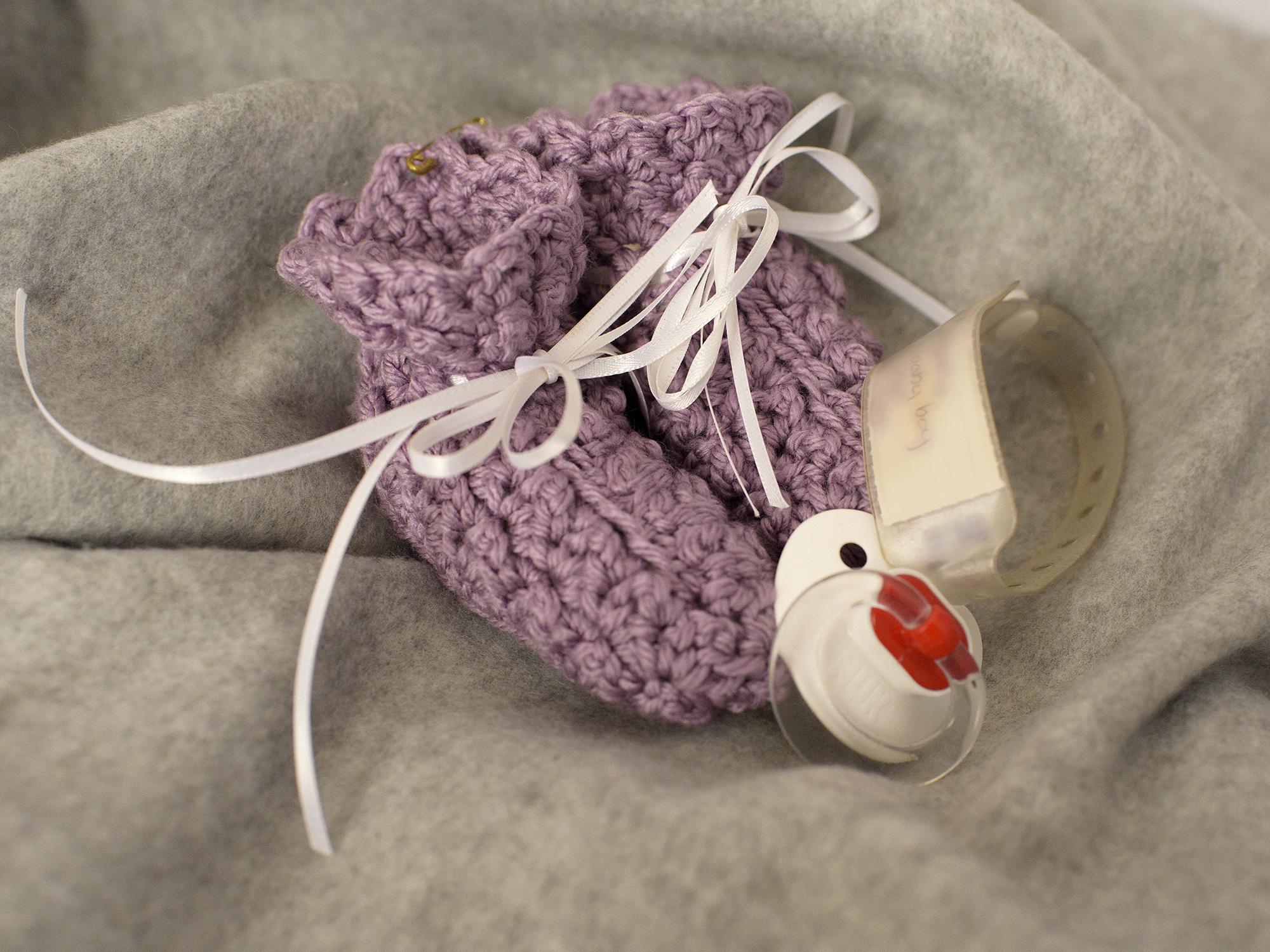 Still life arrangement of a pair of knitted infants booties, a hospital ID band and a pacifier.
