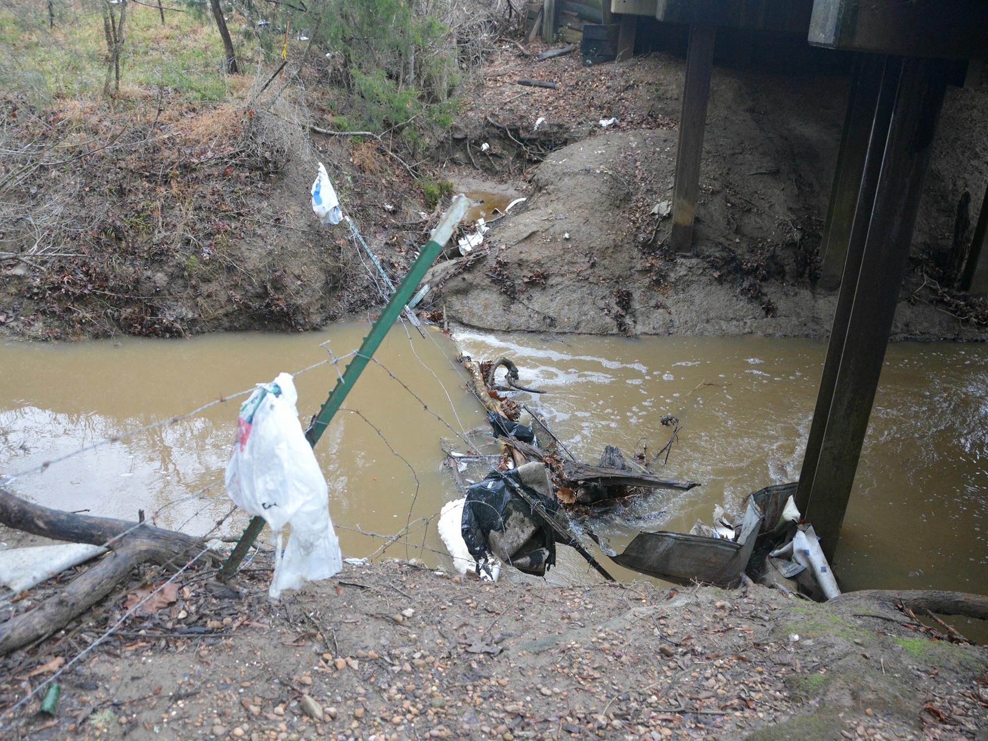 A drainage ditch with moving water, limbs, and trash.