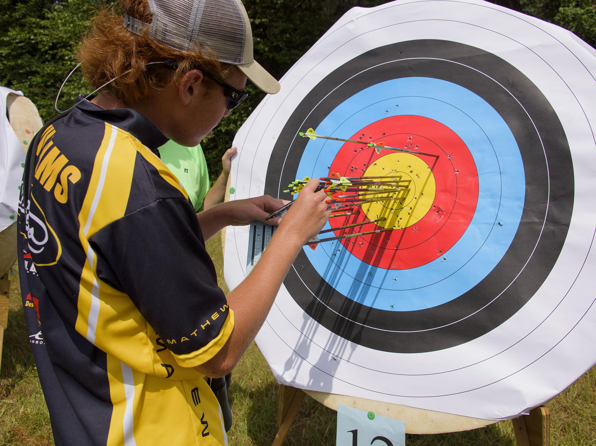 A 4-H’er wearing sunglasses tallies arrows in a colorful paper archery target.