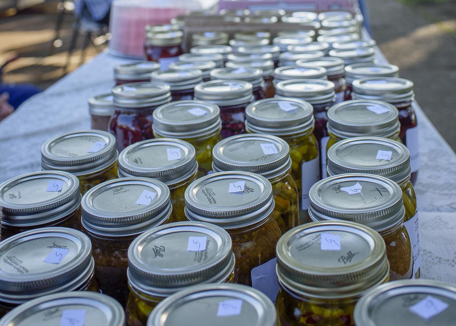 Rows of canning jars line a table at an open-air marketplace.