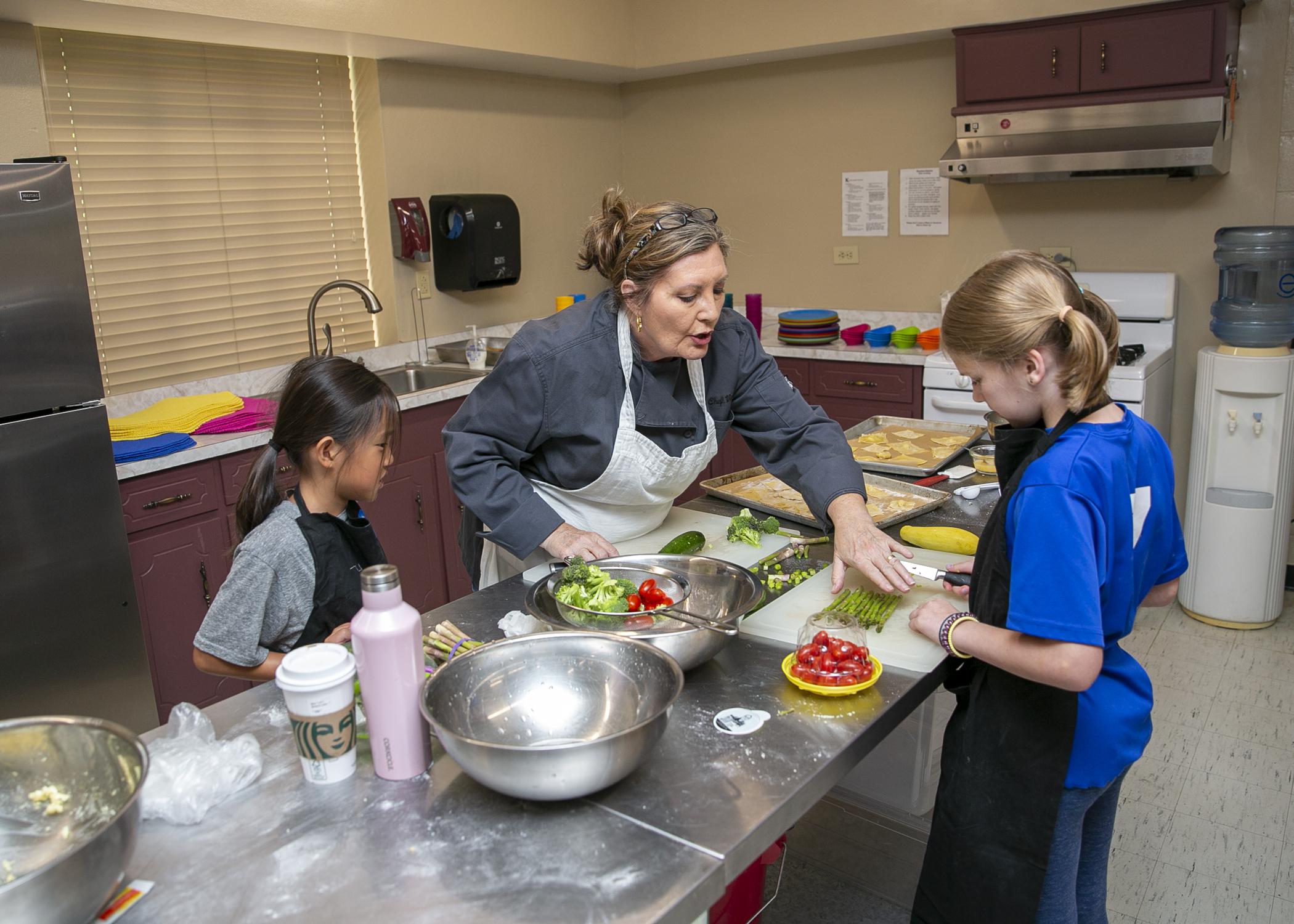  adult instructs two children in a kitchen setting.