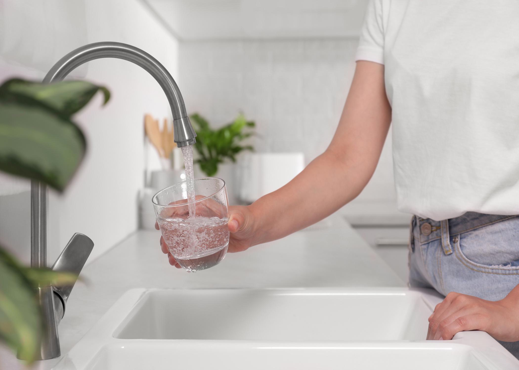 A person fills a glass with water at a kitchen sink.