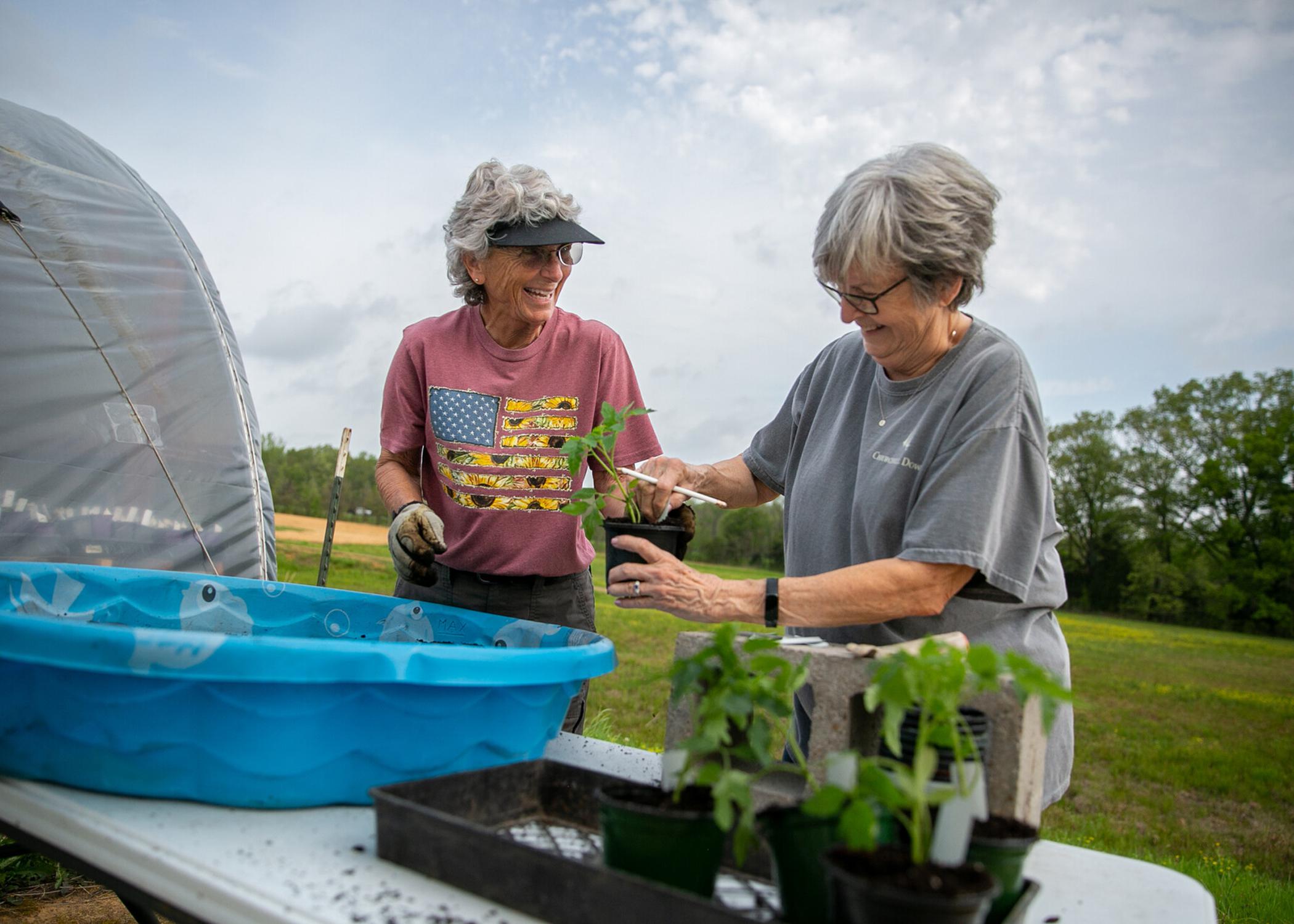 Two women work with potted plants outdoors.