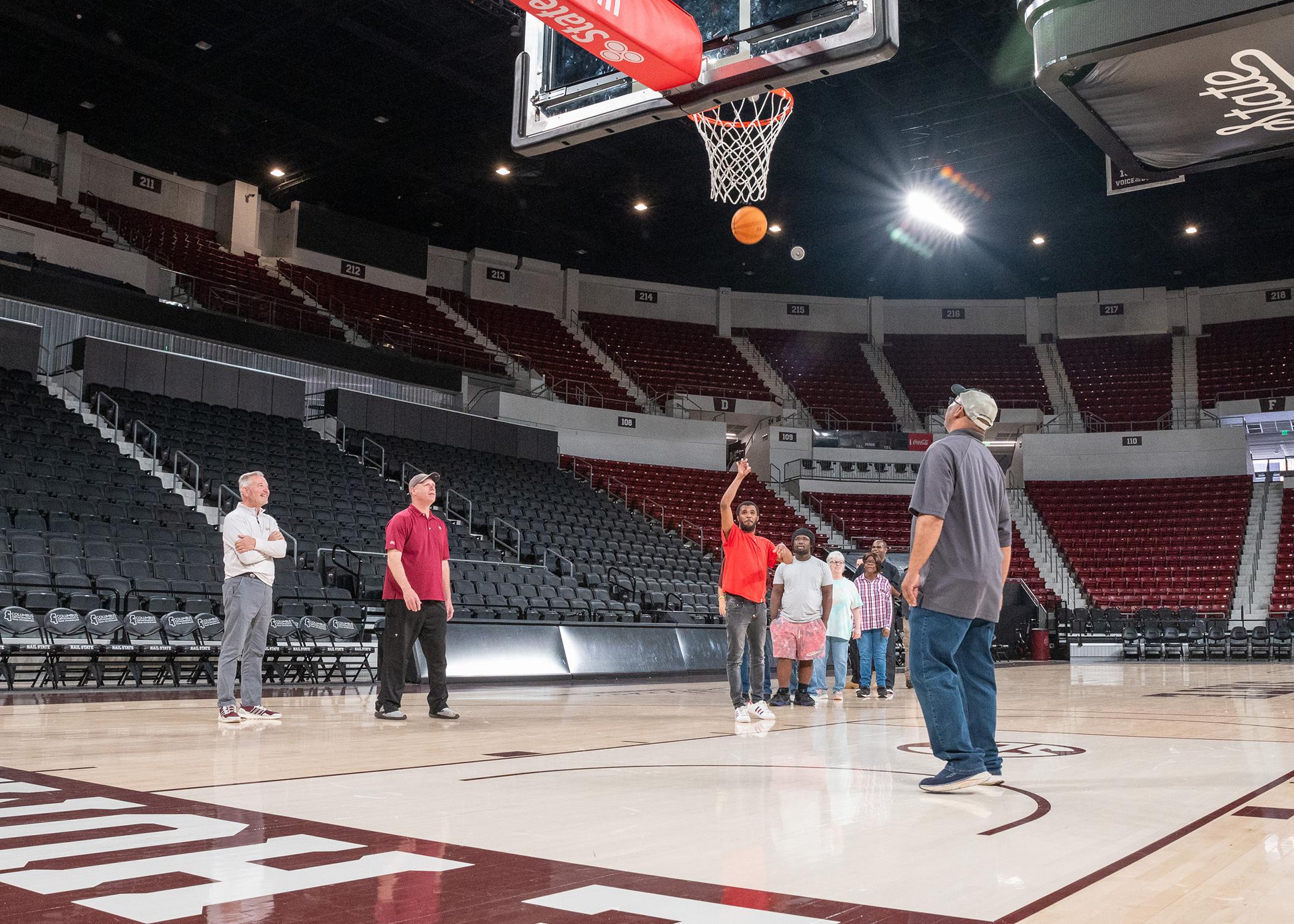 One man shoots a basketball on a court as others stand nearby.