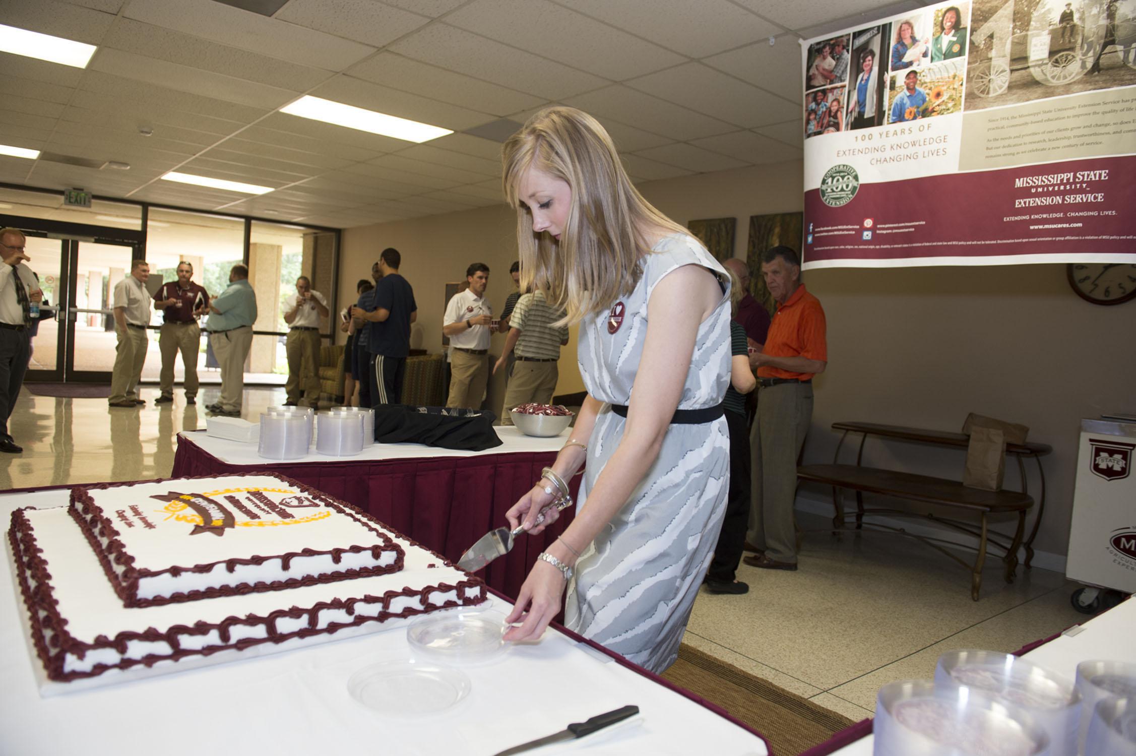 Meaghan Gordon, marketing coordinator at the Mississippi State University Office of Agricultural Communications, cuts the cake May 8, 2014 at the Bost Extension Center that commemorates the 100th anniversary of the Extension Service. Friends of the Extension Service gathered in similar events around the state to celebrate the anniversary. (Photo by MSU Public Affairs/Megan Bean)