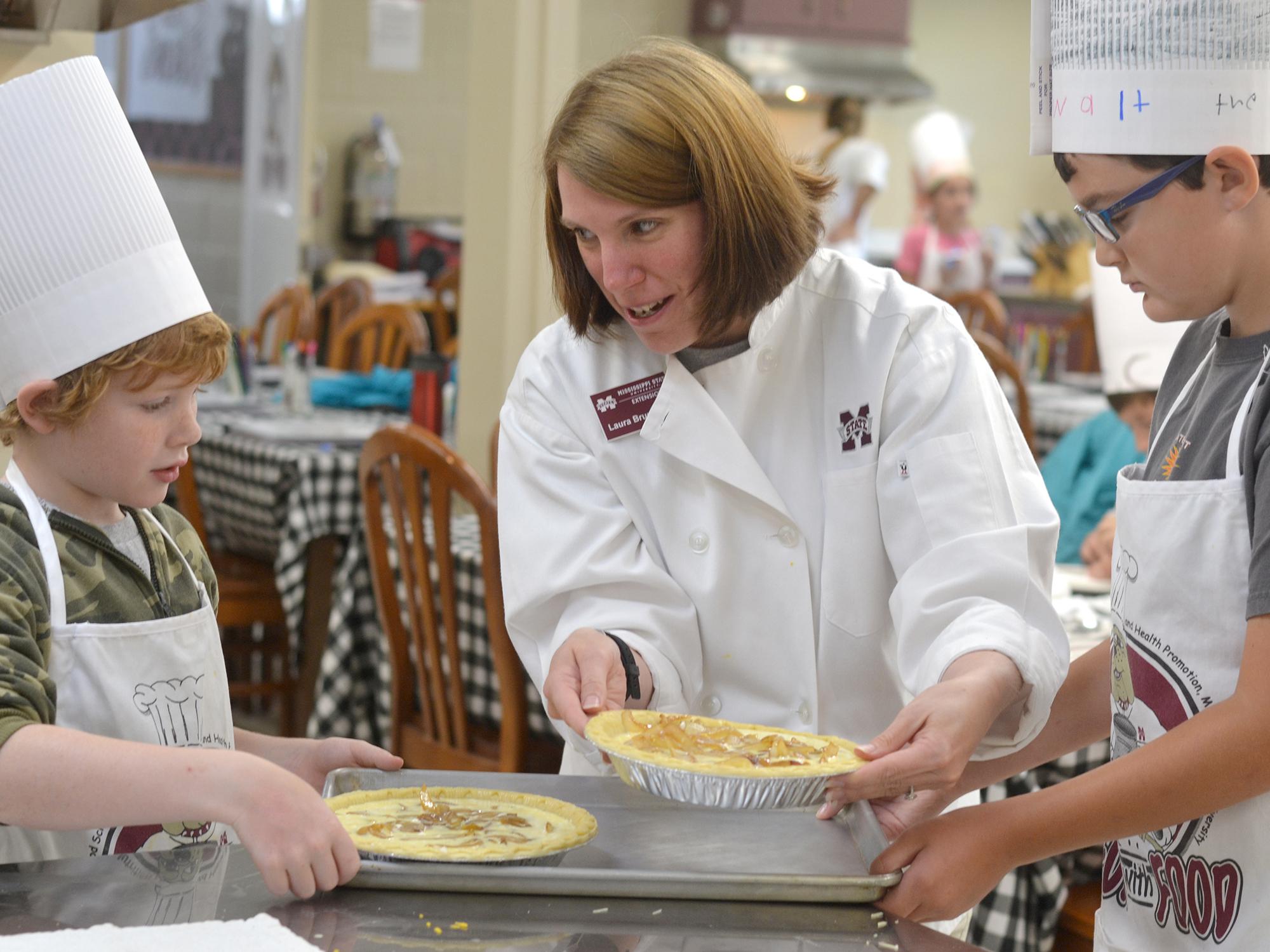 Laura Brumbaugh (center), Mississippi State University Extension Service agent in Tate County, helps Harlan Tagert, left, and Walt Giesen, both of Starkville, finish their quiches on June 21, 2016, at the MSU Fun with Food Camp. The annual summer camp offers hands-on training and educational field trips for 3rd- to 6th-grade children to learn about nutrition, cooking and food safety. (Photo by MSU Extension Service/Michaela Parker) 