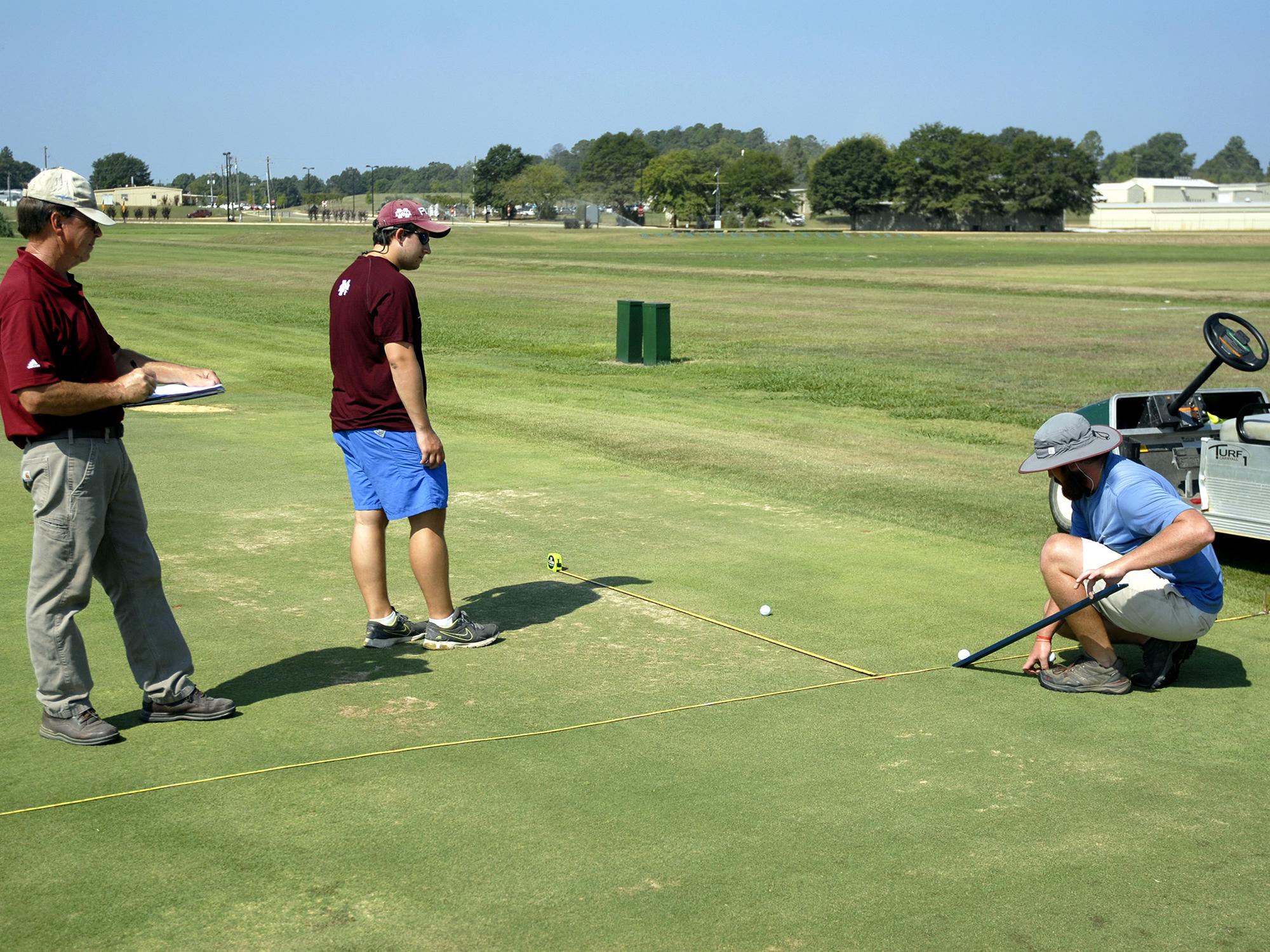 Mississippi State University Department of Plant and Soil Sciences senior research associate Wayne Philley, left, and MSU seniors Abram Diaz of D’Iberville and Aaron Tucker of Carthage measure how far a golf ball rolls over different varieties of bermudagrass at the R. R. Foil Plant Science Research Center Sept. 4, 2015. (Photo by MSU Ag Communications/Nathan Gregory)