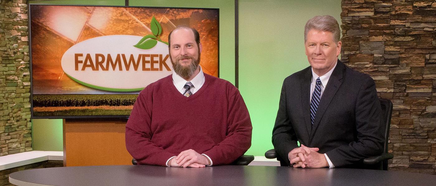 Two men sit at a TV studio desk with Farmweek logo on monitor behind him.