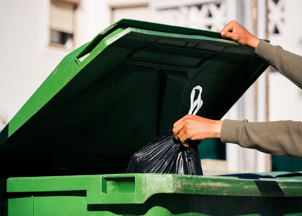 A person throwing a trash bag into a trash can.