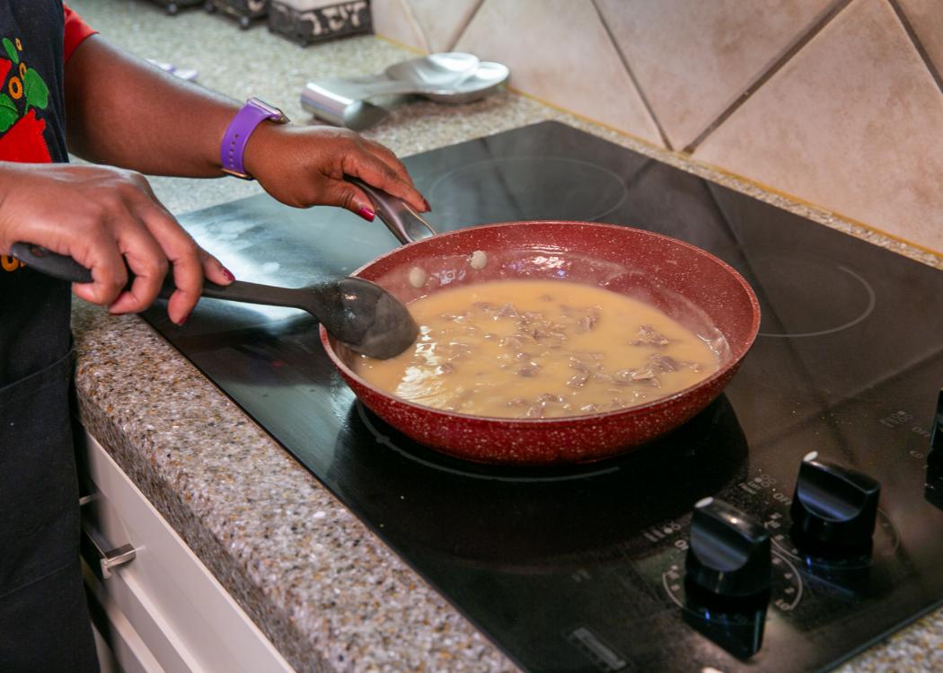 A person stirs a skillet of turkey gravy cooking on the stove.